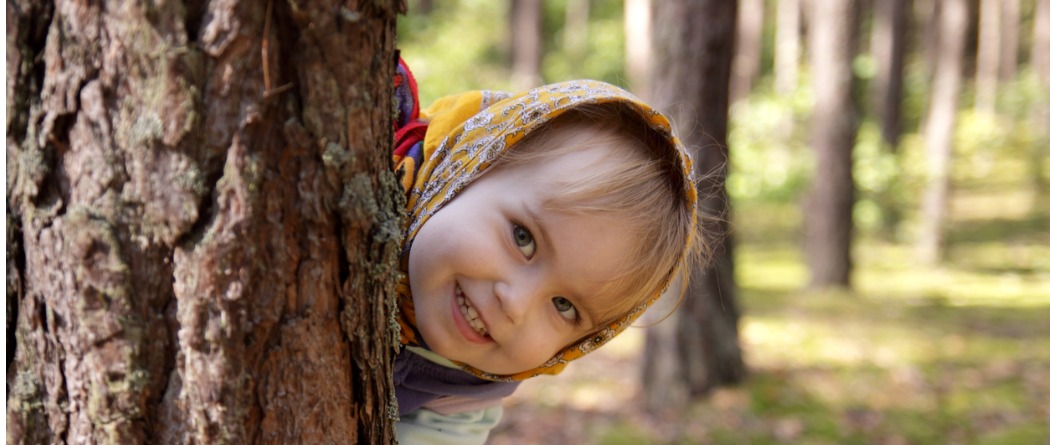 Little girl peeking around a tree trunk