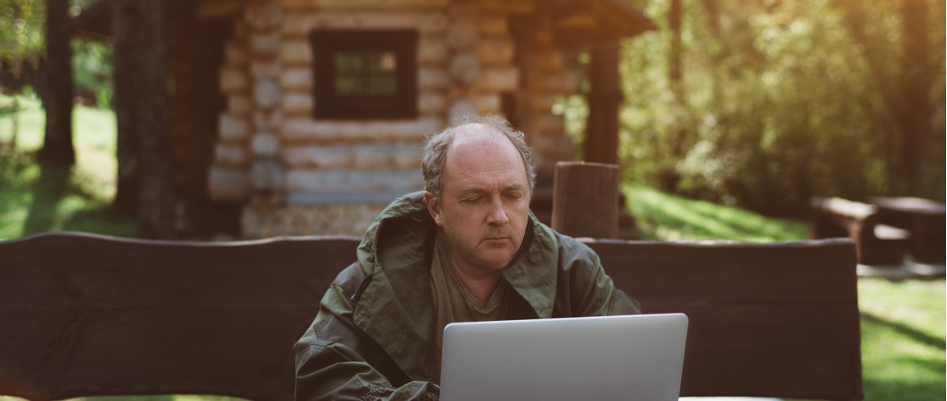 An man sitting outside on a park bench on a brisk cool day working on his laptop.