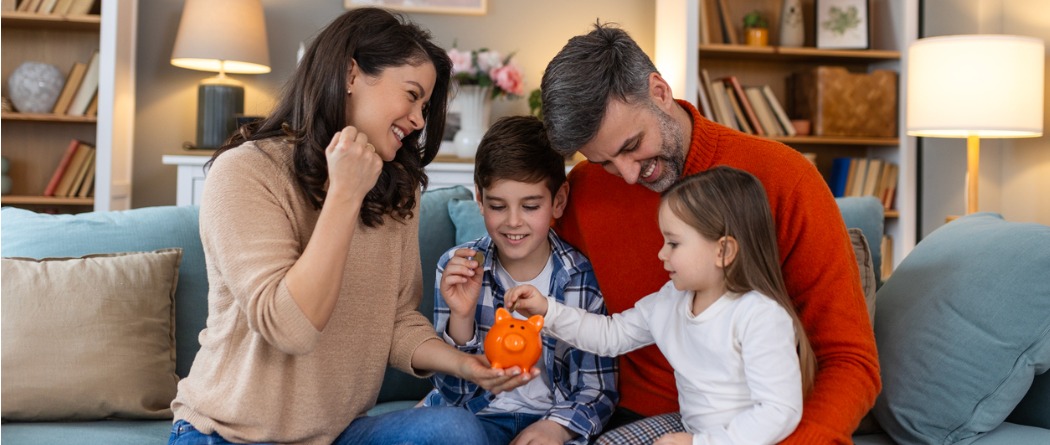 Happy family sitting on couch putting money in a piggy bank