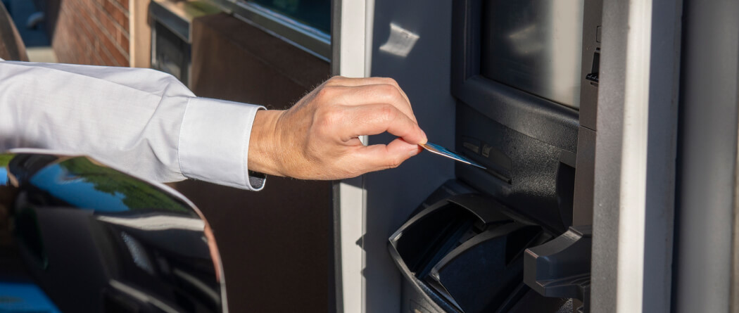 close-up of a hand placing a debit card into an ATM machine