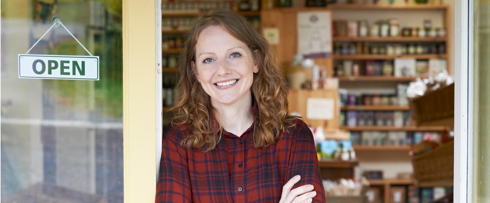A picture of a business owner standing in front of her shop next to an open sign