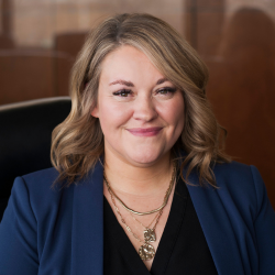 A young blond woman in business style dress is sitting in an office chair.
