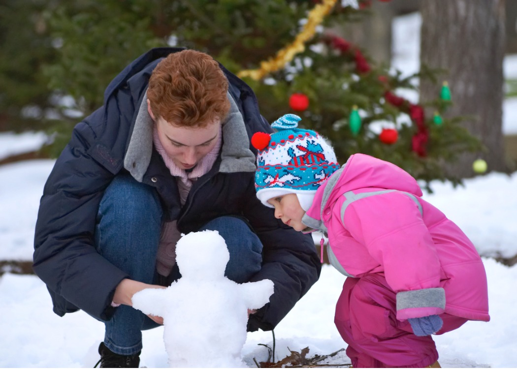 Woman and child building a small snowman together outside.