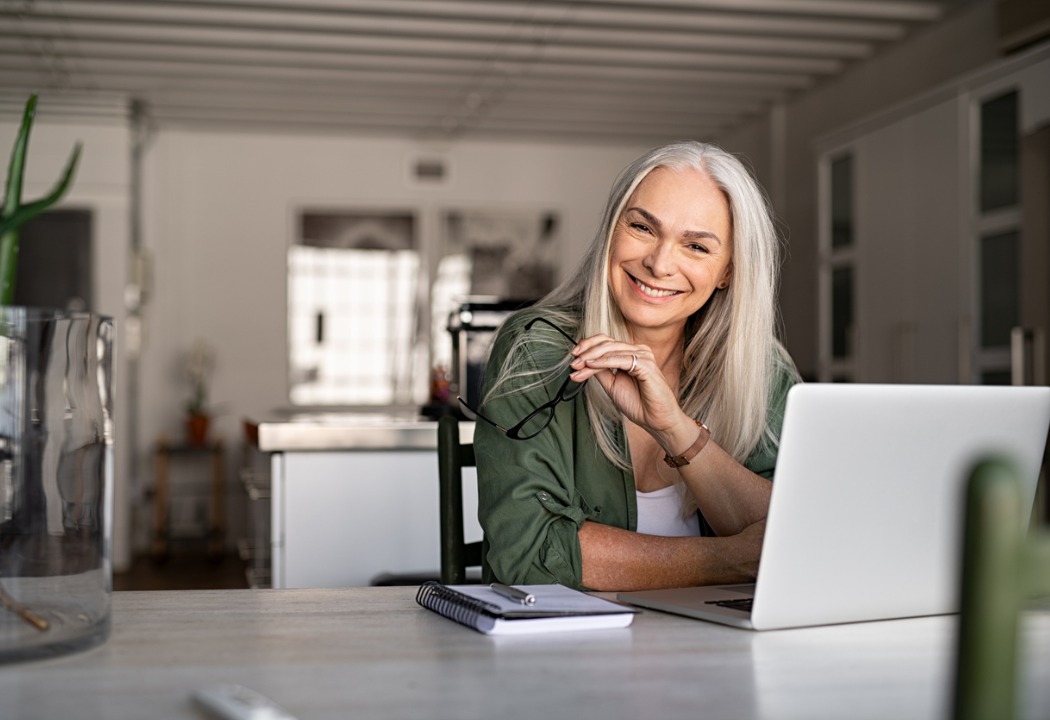 Confident older lady smiling at her table with her laptop.