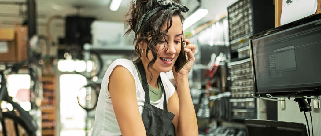 Woman working in a bike shop talking on a smartphone