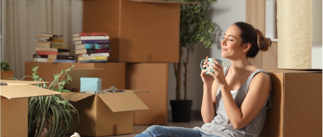 A young woman enjoying a warm cup of coffee while she takes a break from unpacking in her new home.