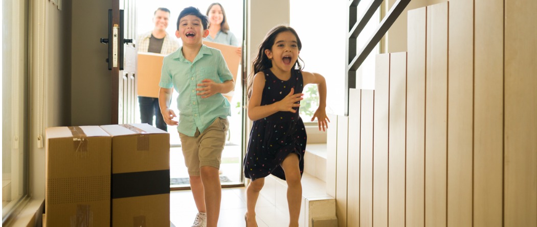 Two excited young children running through the front door of their new house on moving day.