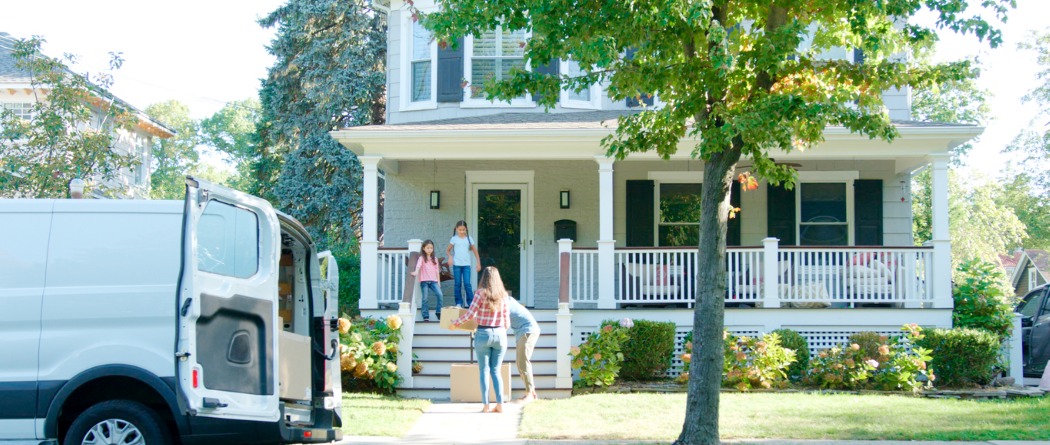 A family on the front steps of their beautiful new home after unloading boxes from a moving van.