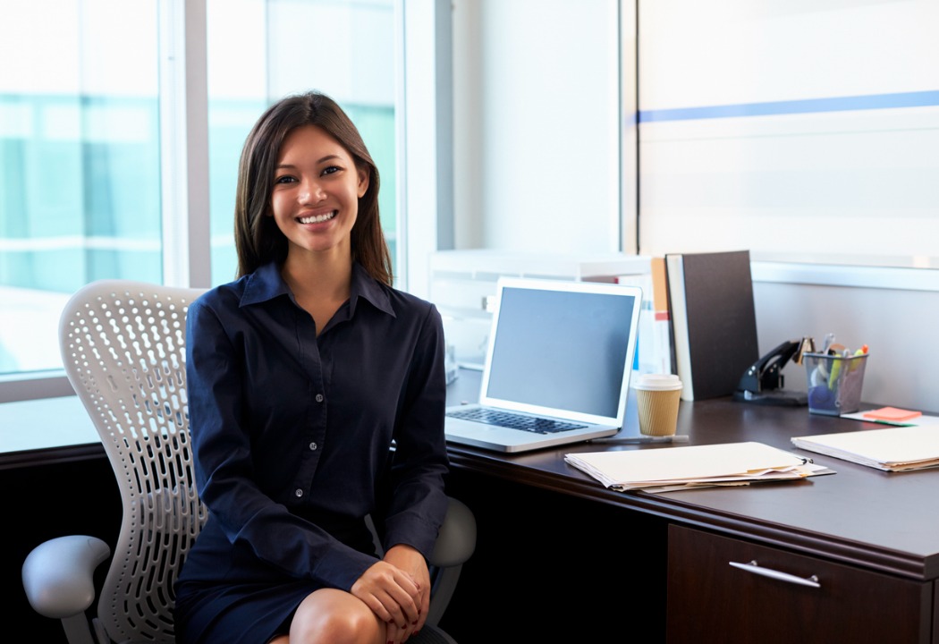 A picture of a woman smiling at the camera and sitting at her desk
